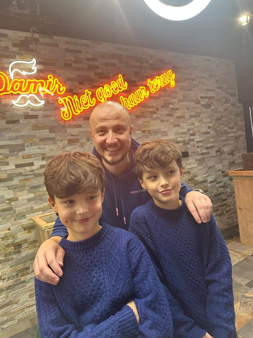 Damir in de zaak, met zijn twee zoontjes voor de neonwand